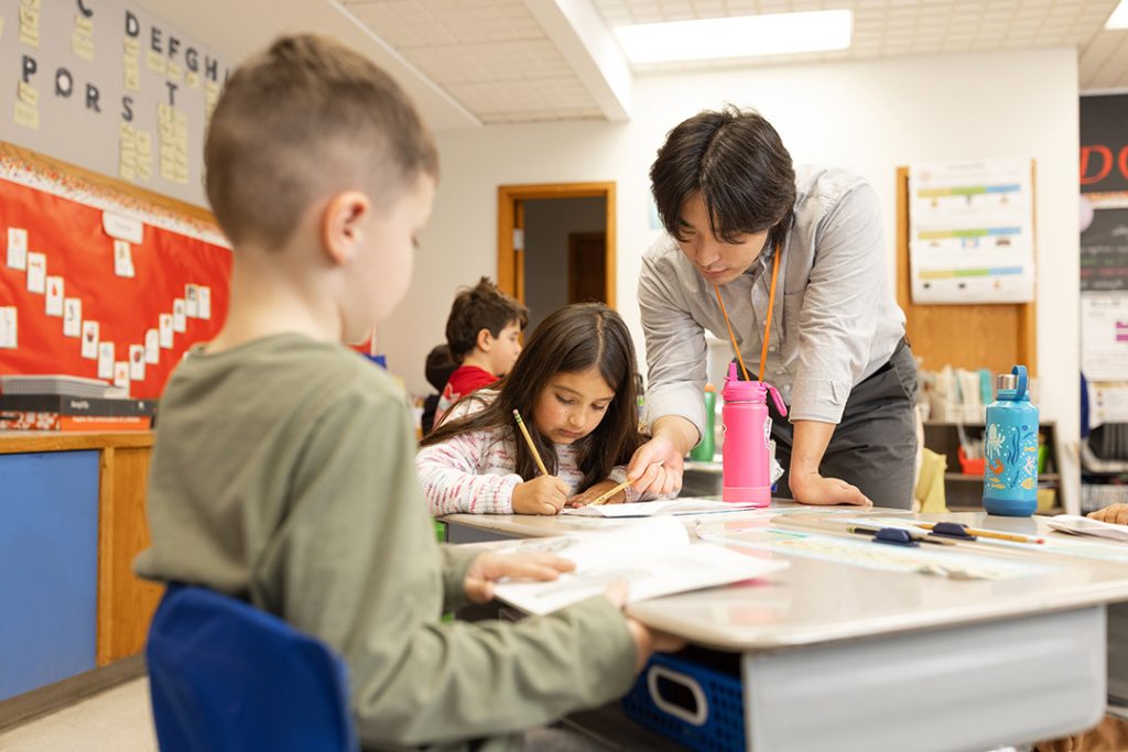 A man works with young students at an elementary school 
